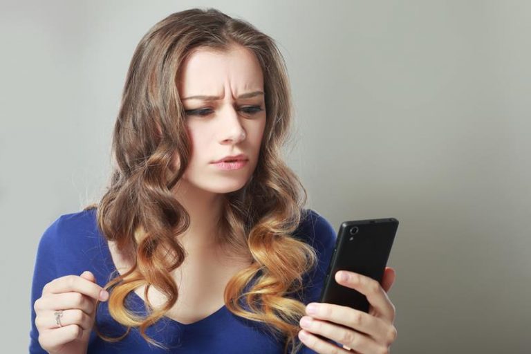 a young woman looking at her phone with an inquiring expression